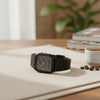 Cassims&Co. Casio ana-digi watch with a grey dial, gold indices, and black resin strap on a desk with coffee beans.