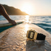 Cassims&Co. Casio F-91WM gold-tone digital watch with black resin strap resting on a surfboard at sunset