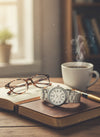 Cassims&Co. Casio quartz watch with white dial and stainless steel bracelet resting on a book with glasses and coffee