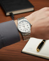 Cassims&Co. Casio quartz watch with a white dial, Arabic numerals, and stainless steel bracelet on a wrist.