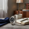 Cassims&Co. Casio stainless steel watch with black dial, Roman numerals, and date window on a desk with a notebook.