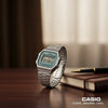 Cassims&Co. Casio Vintage digital watch with a green dial and stainless steel bracelet on a wooden desk.