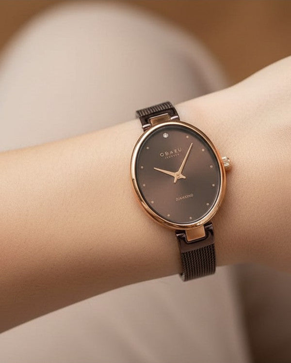 Cassims&Co. Obaku Denmark oval ladies watch with rose gold case, brown dial, diamond accent, and mesh strap on wrist