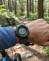 Cassims&Co. Casio G-Shock GD-010-3 green resin digital watch worn on a wrist while mountain biking in a forest.