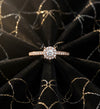 Cassims&Co. 9ct rose gold engagement ring featuring a round diamond halo and pavé-set band on black velvet fabric.